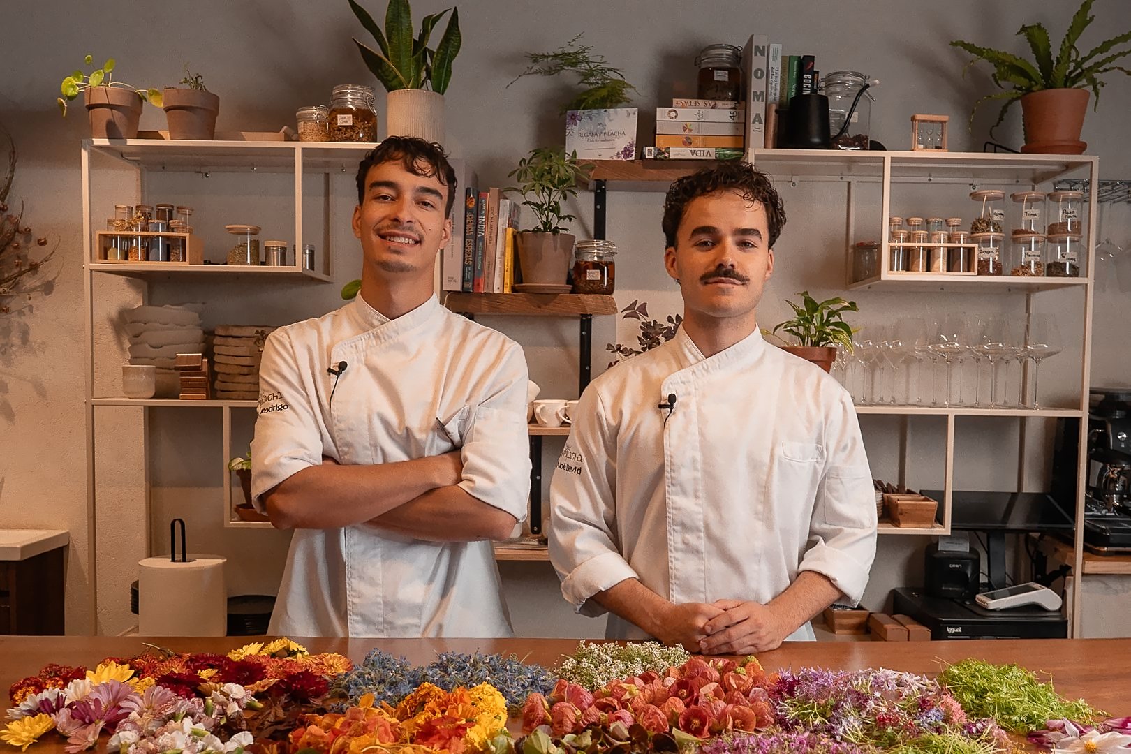 Arán y Noé tras la barra de Pipilacha, con flores comestibles extendidas sobre la madera